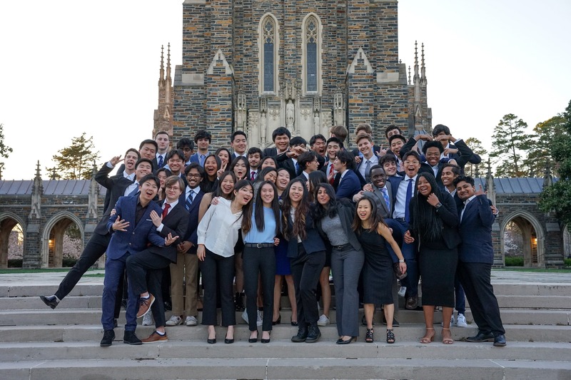 A large group posing together on the steps outside a stone chapel.