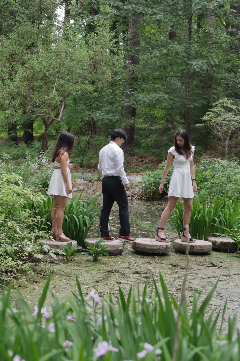 Three people on stepping stones beside a pond in a leafy woodland.